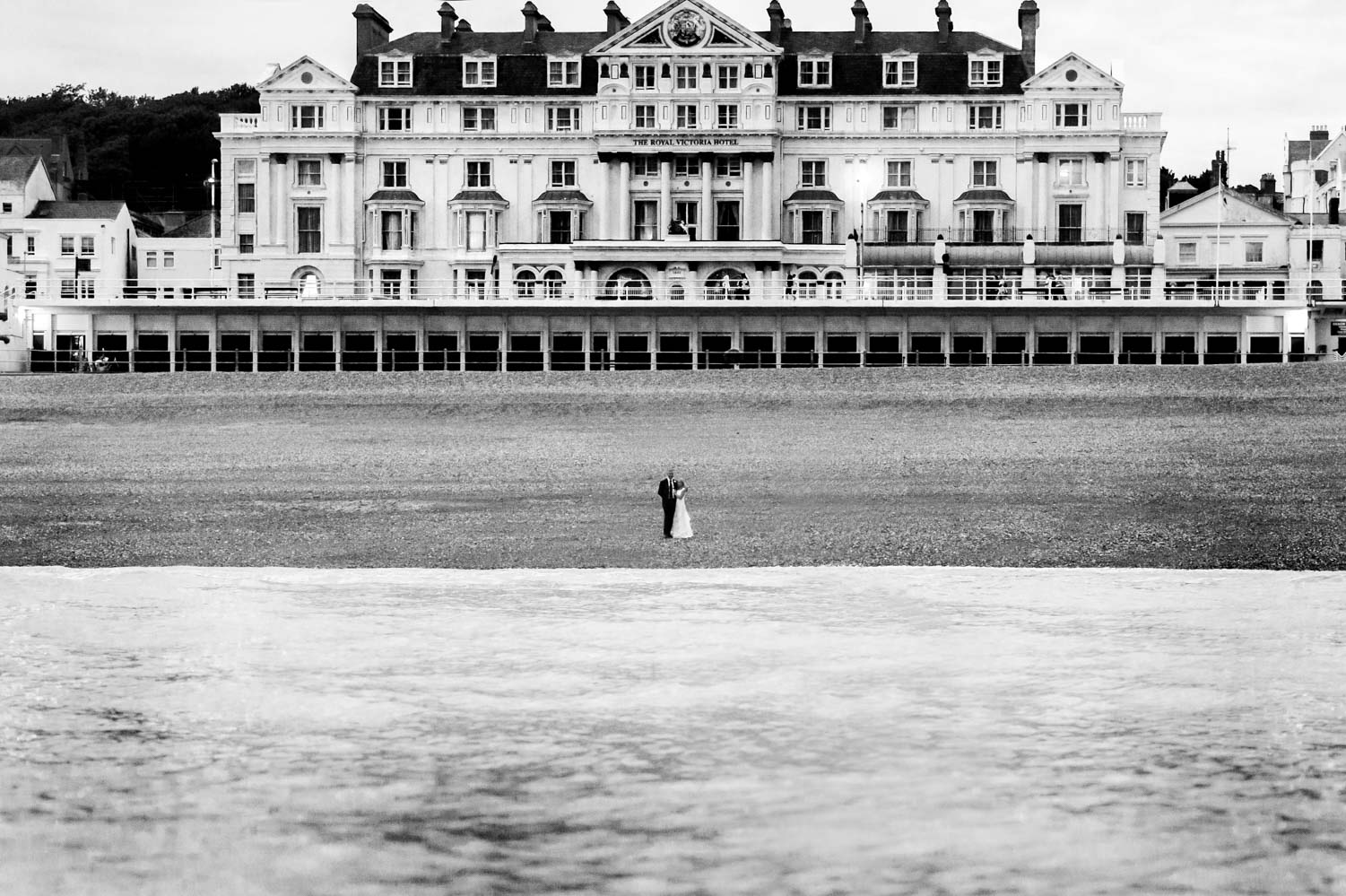 Bride and groom on Hastings beach photographed from the sea by informal Sussex wedding photographer James Robertshaw