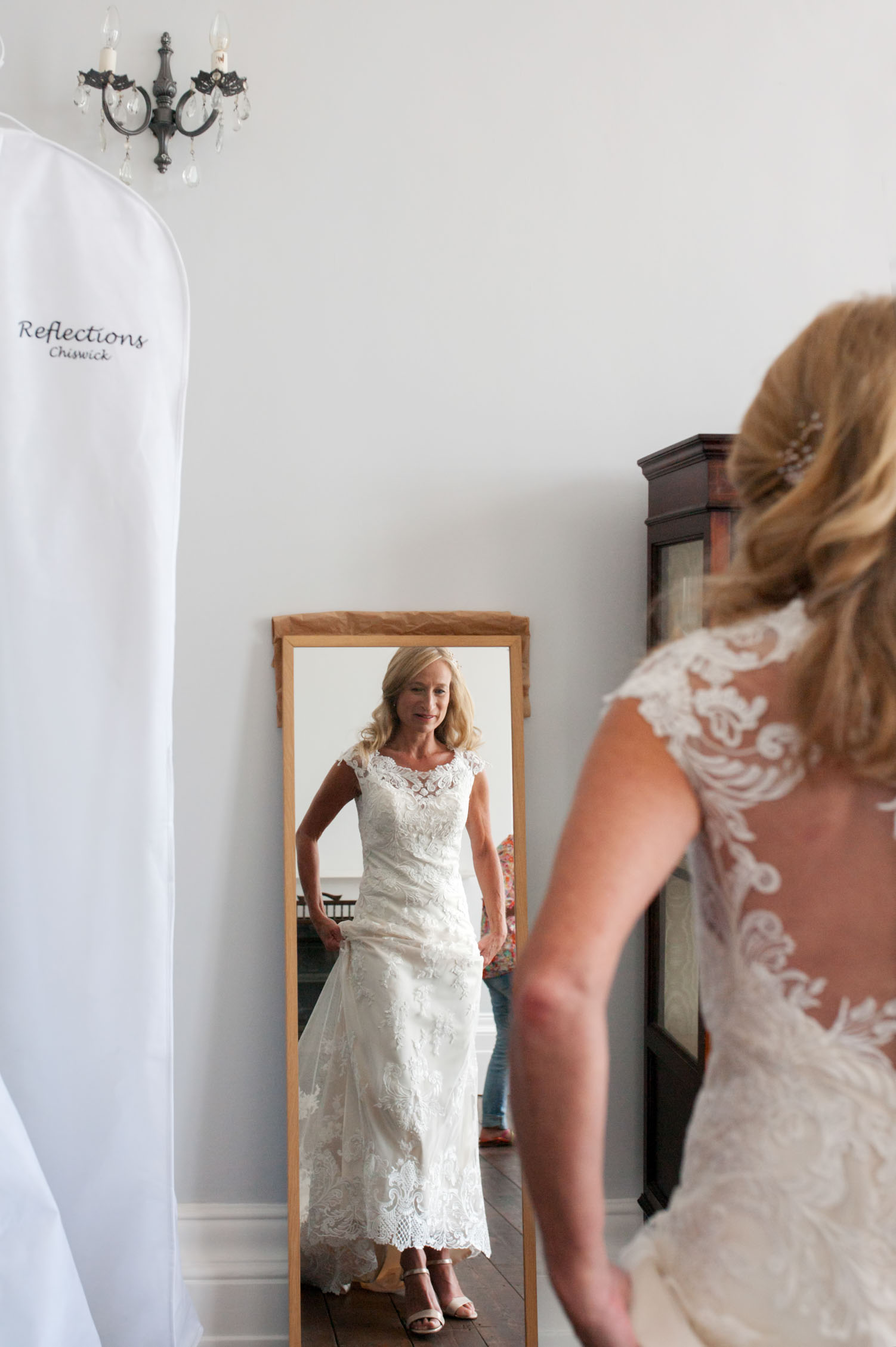 Bride in dress looking in full length mirror by informal Sussex wedding photographer James Robertshaw