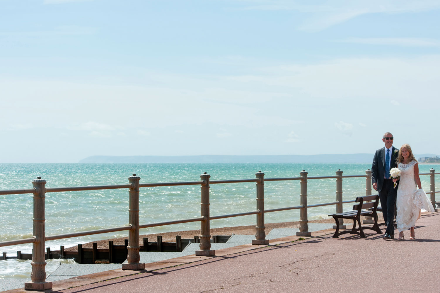 Bride and groom walking along  Hastings seafront by informal Sussex wedding photographer James Robertshaw 