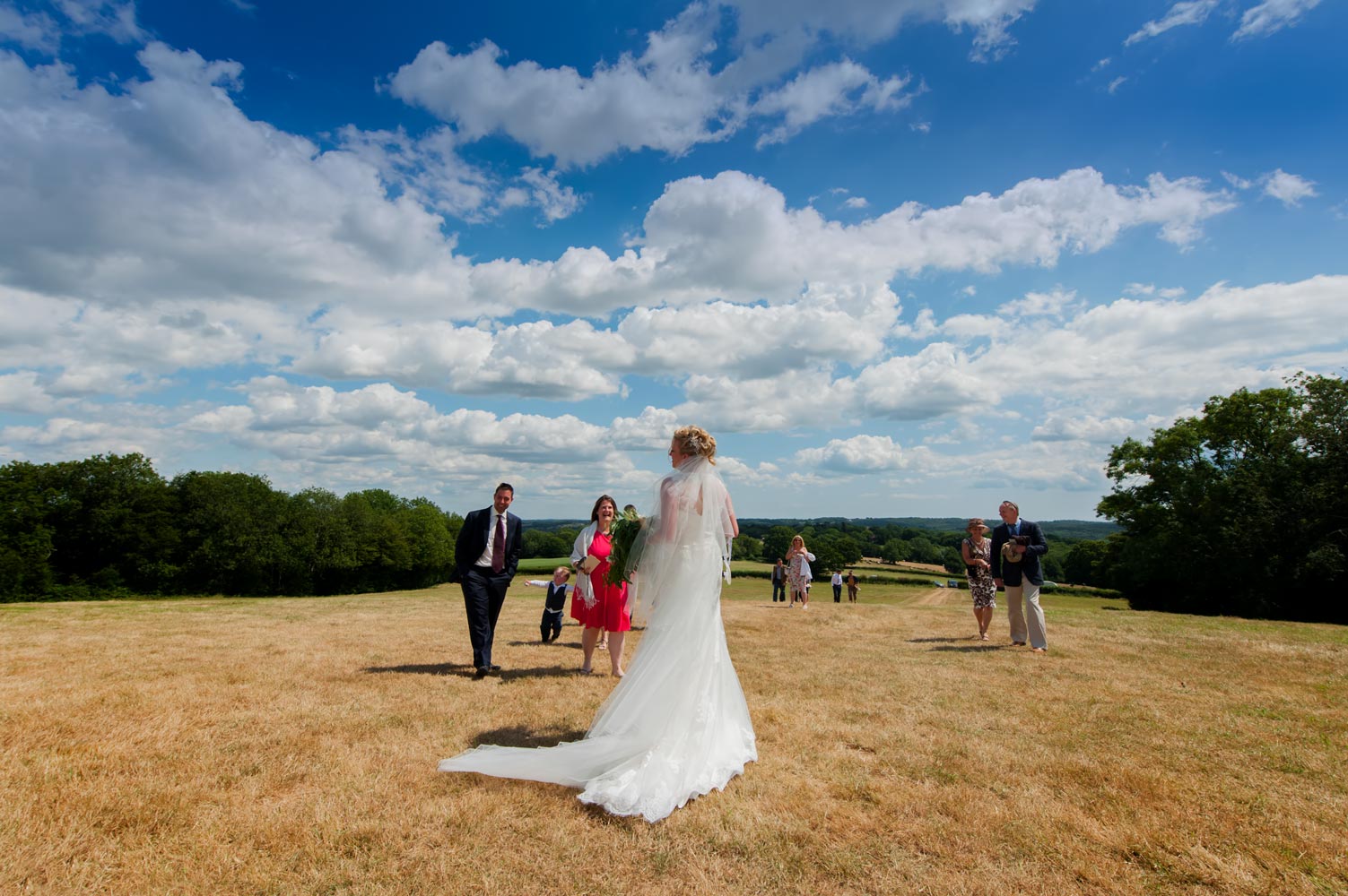 Bride on hillside greeting wedding guests