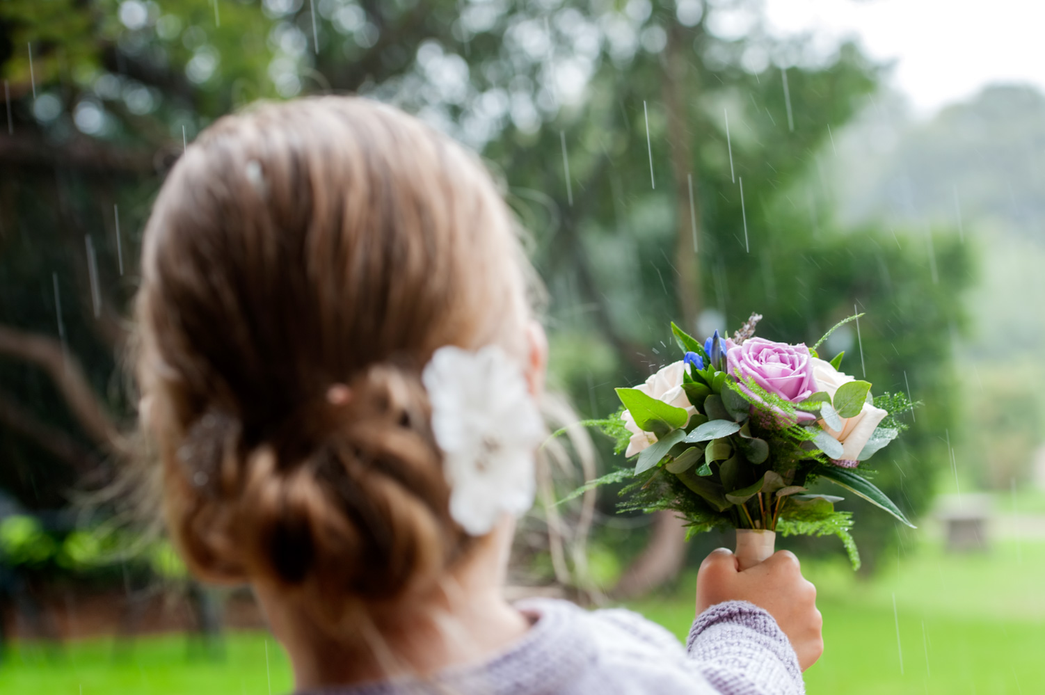 Bridesmaid holding bouquet out to catch raindrops