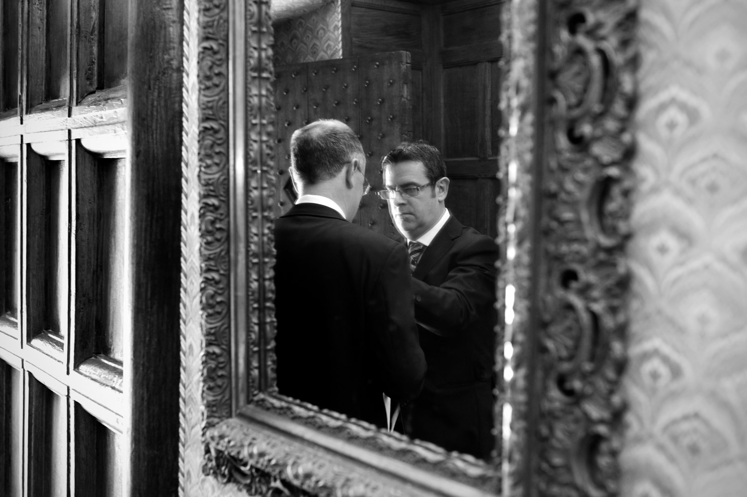 Best man fixing Groom's tie reflected in mirror