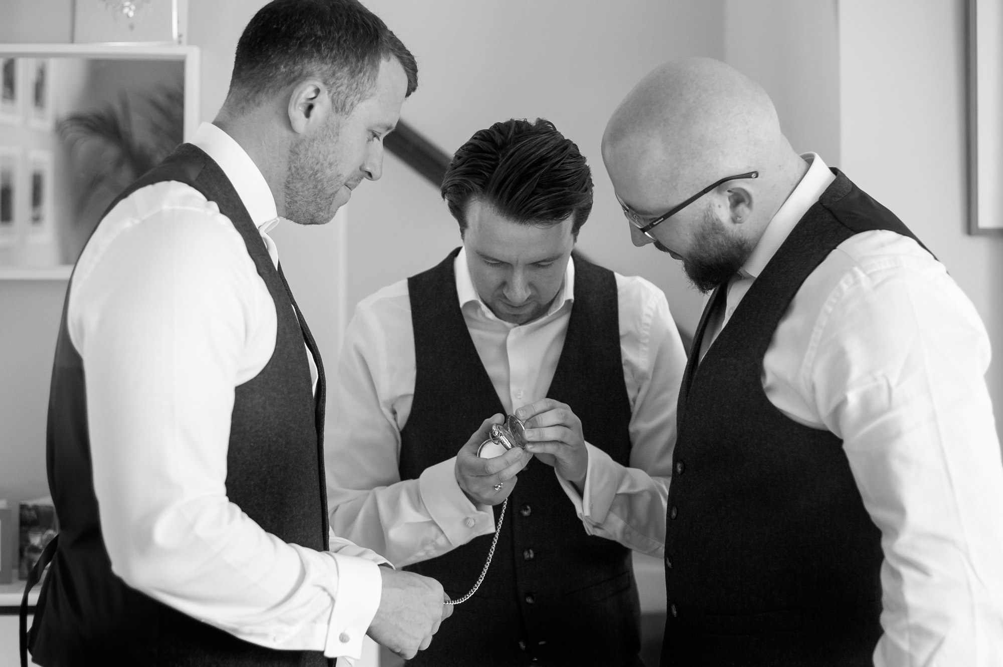 Groom and brothers looking at pocket watch by West Sussex wedding photographer James Robertshaw. 