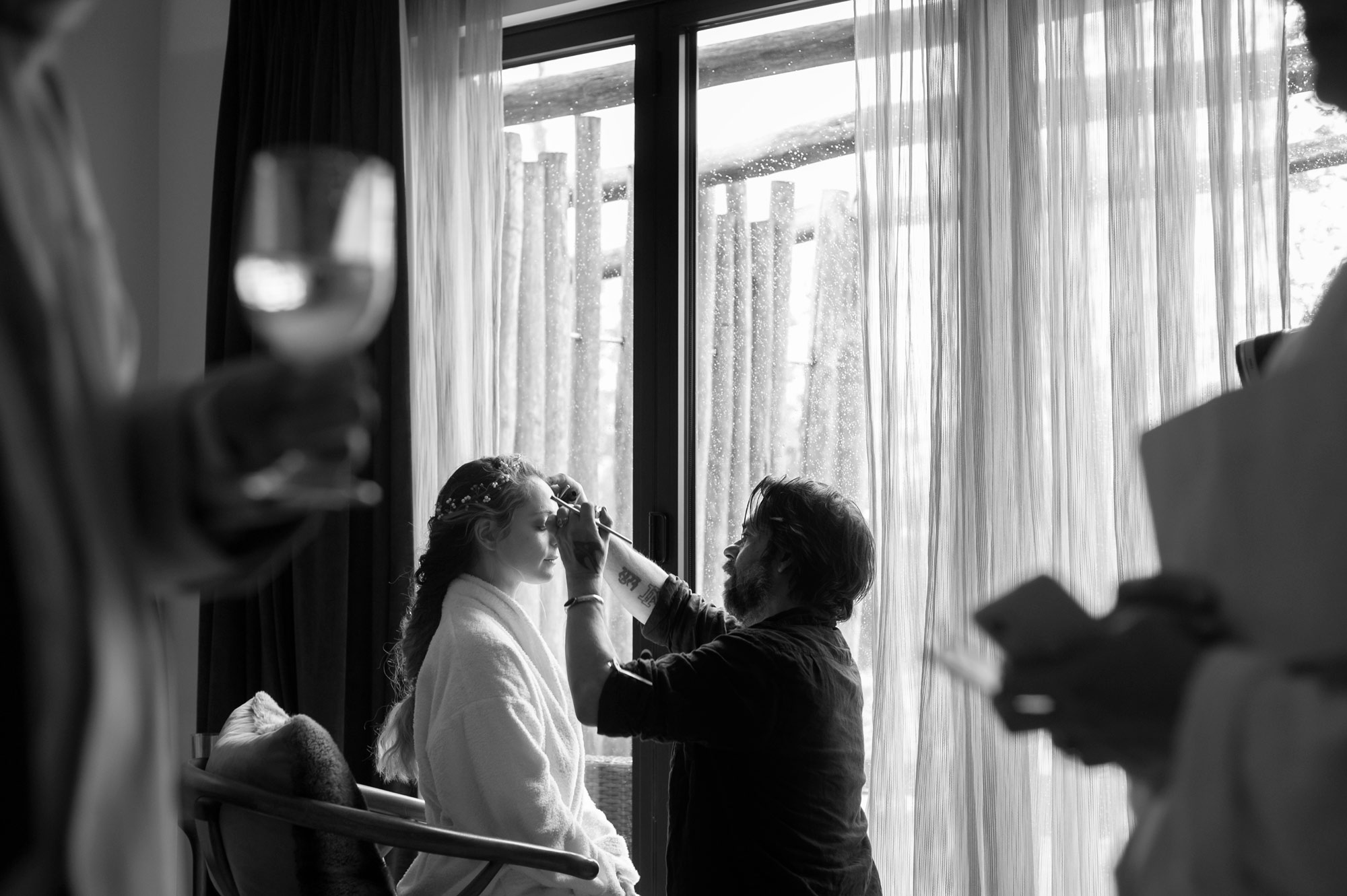 Bride having make up done framed by two people talking by West Sussex wedding photographer James Robertshaw.