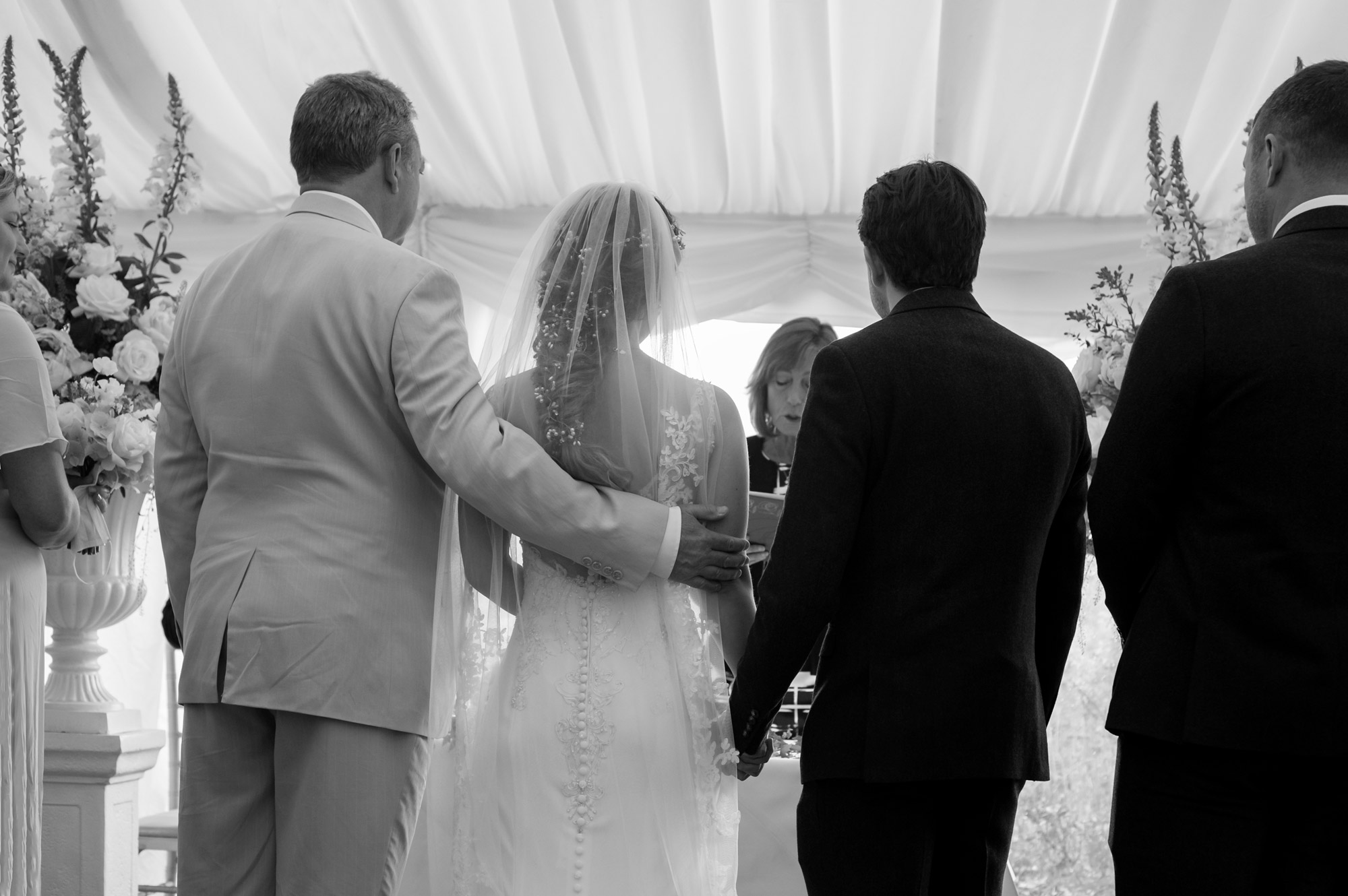 Father with arm round bride who is holding hands with groom. 