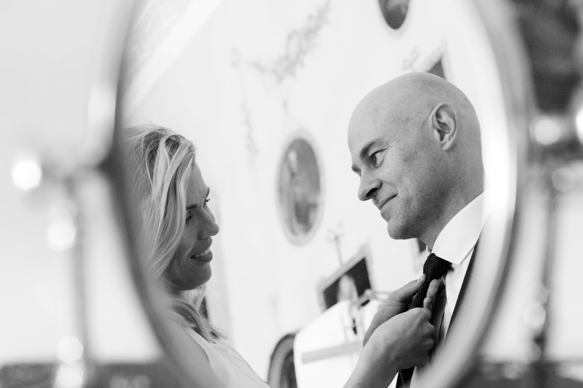 Bride tieing husband's tie reflected in a mirror 