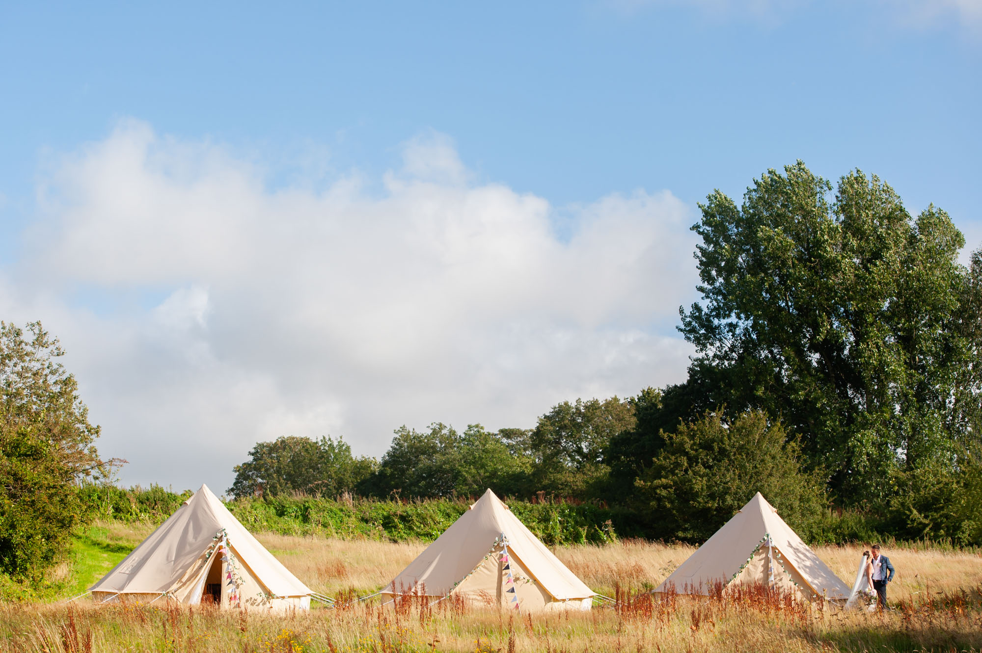 Bride and groom in field with bell tents by East Sussex documentary wedding photographer James Robertshaw.