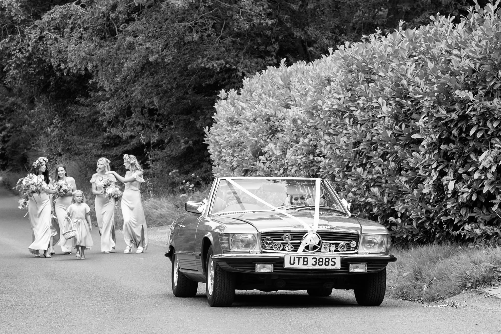 Father driving daughter to wedding followed by bridemaids on foot.