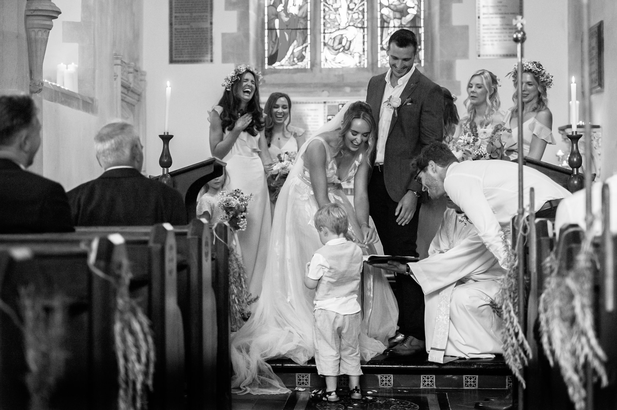 Wedding party laughing with young ring bearer during ceremony.