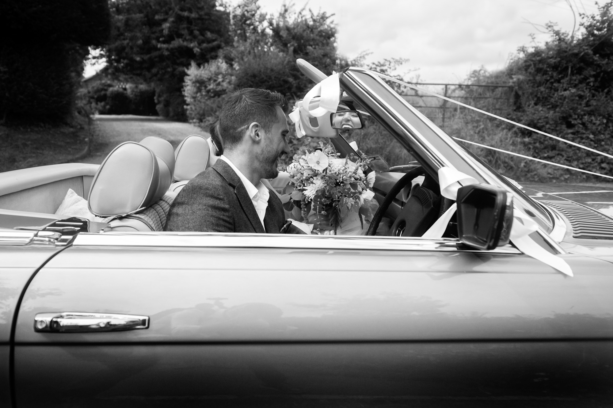 Bride laughing relfected in car rear view mirror.